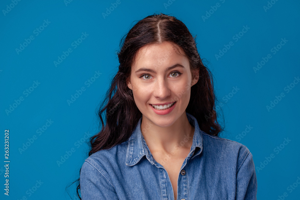 Close-up portrait of an attractive brunette girl with long curly hair posing on a blue background. Close-up portrait of an attractive brunette girl with long curly hair posing on a blue background.