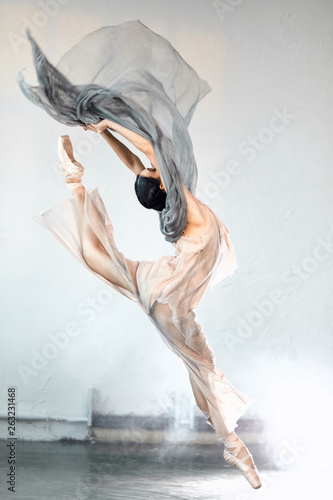 Fotografie Adorable dar-haired female dancer performing on scene her part of concert jumping high in the air expressing emotions and beauty of classical ballet