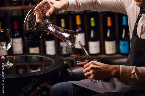 Skilled sommelier pouring wine from decanter into wine glass. Degustation of wine process in wine boutique, close up.