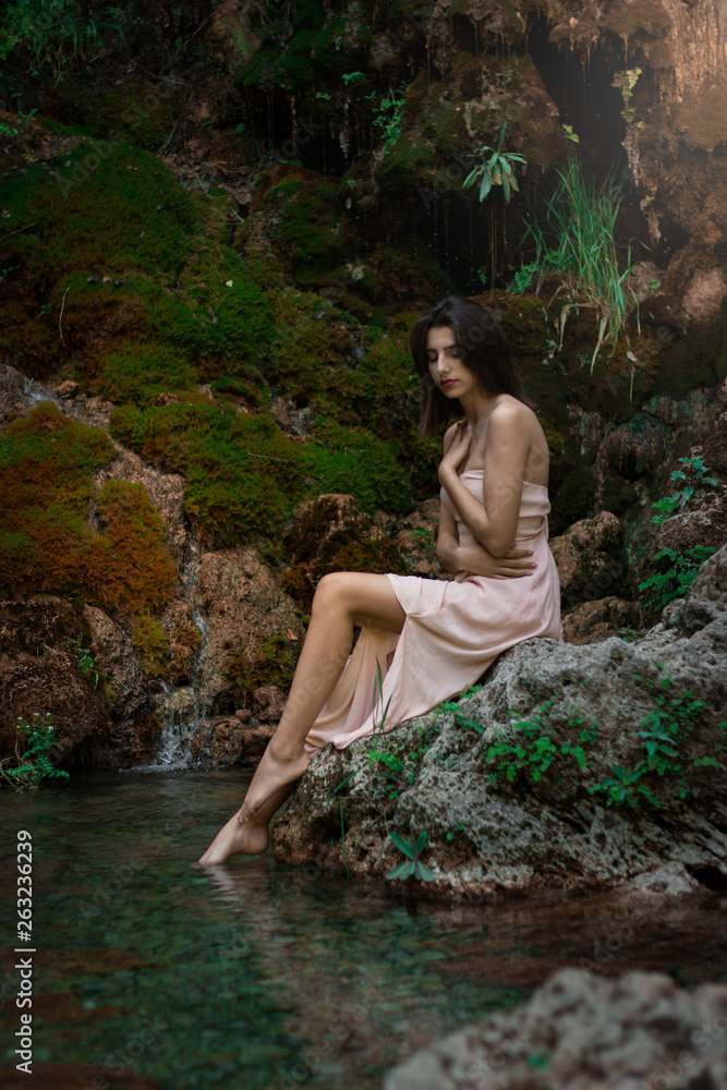 Fototapeta premium Beautiful girl posing in river. Fairytale story. Natural pool surrounded by green tree's leafs.