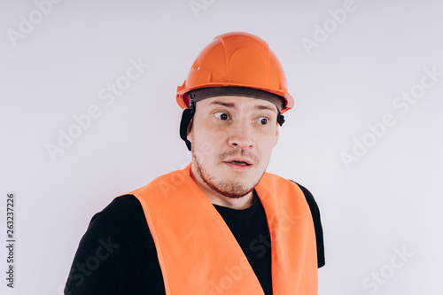 Man in working uniform on white background Portrait of young male in bright orange protective hardhat and vest looking at camera on white background