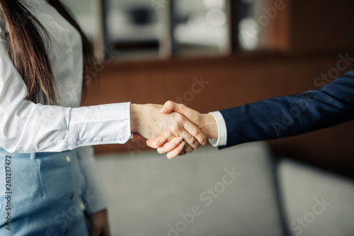 Two caucasian businesswomen in office clothes shaking hands at the meeting as they close a partnership, focus on hands