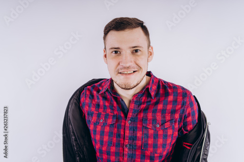 Cool man with jacket on shoulder Portrait of young handsome male in red plaid shirt holding leather jacket on shoulder against white background