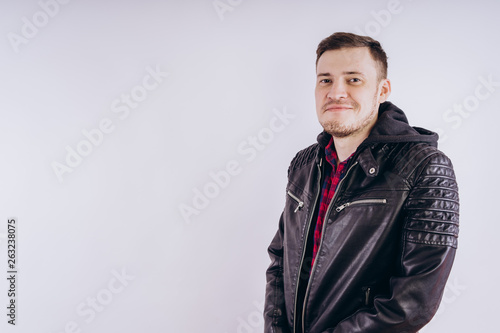 Man in trendy jacket on white background. Portrait of young male in leather jacket zipping up and smiling at camera on white background