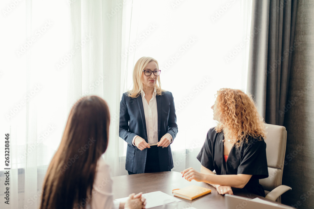 Group of business women meeting at the office. Blonde woman dressed in formal suit sharing her ideas with two colleagues, sitting at the desk. Group of business women meeting at the office. Blonde woman dressed in formal suit sharing her ideas with two colleagues, sitting at the desk.