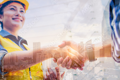 Double exposure engineering and construction concept. Industrial engineer wear safety helmet shaking hands meeting for architectural project working with partner and smile with city background. photo