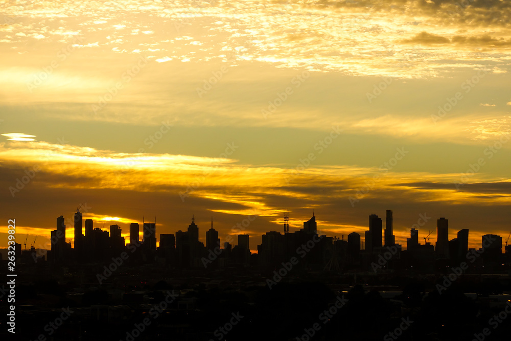 Silhouette of Melbourne city landscape against dramatic golden yellow clouds before sunrise in the early morning. VIC Australia