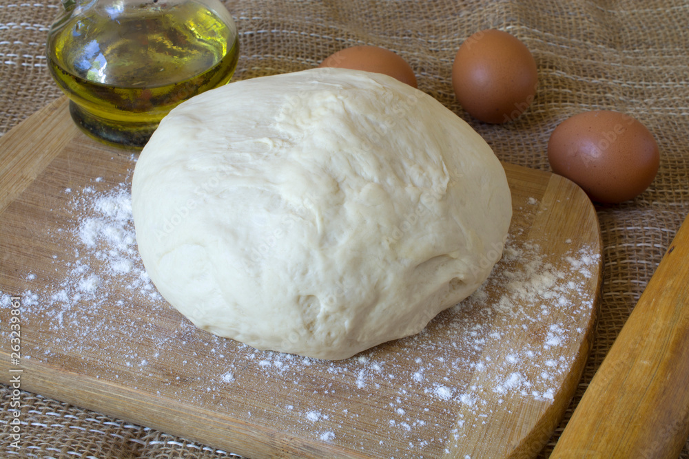 Fresh raw dough in a glass bowl on a wooden board with eggs and oil. Fresh raw dough in a glass bowl on a wooden board with eggs and oil.
