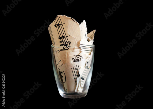 фотографія Torn musical notes in a glass, pieces of paper, isolated on black background