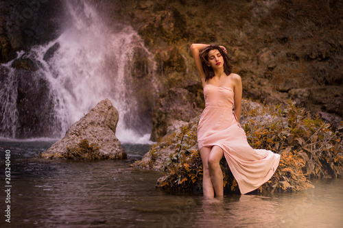 Fototapeta Naklejka Na Ścianę i Meble -  Attractive girl posing on the rock among in fairy fast forest in autumn and beside beautiful waterfall with blue water. Fairy tale.