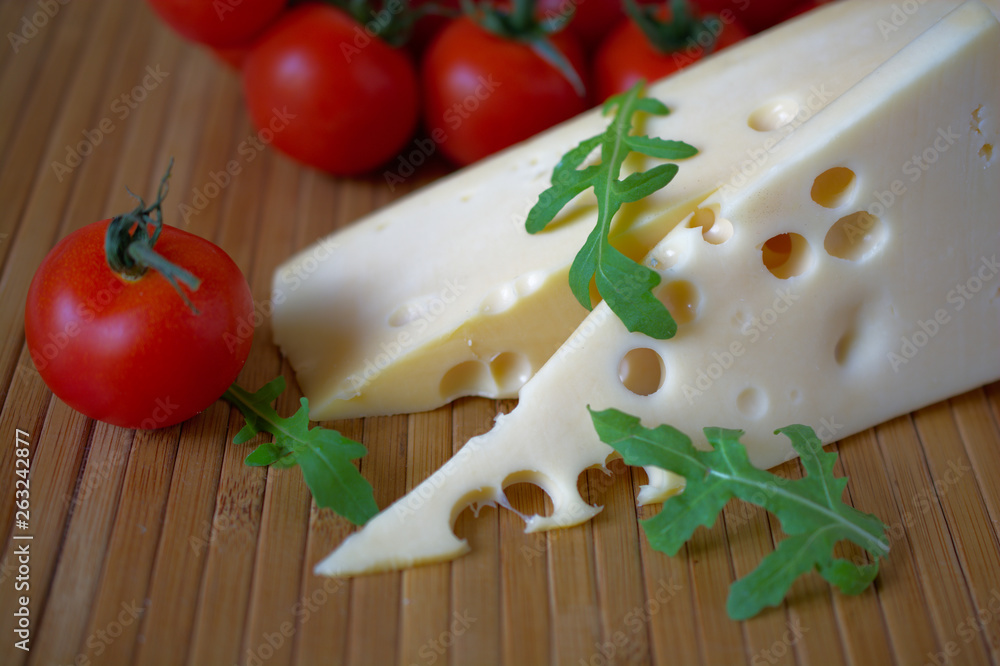 Slice of cheese with tomatoes and herbs on wooden mat.