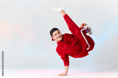 Billede på lærred Stylish dressed in red sweatpants asian b-boy is performing kick in air, standing on hands while dancing break dance on white background