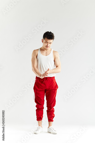 Studio portrait of Korean gymnast in white undershirt and red sweatpants looking at camera over white background © alfa27