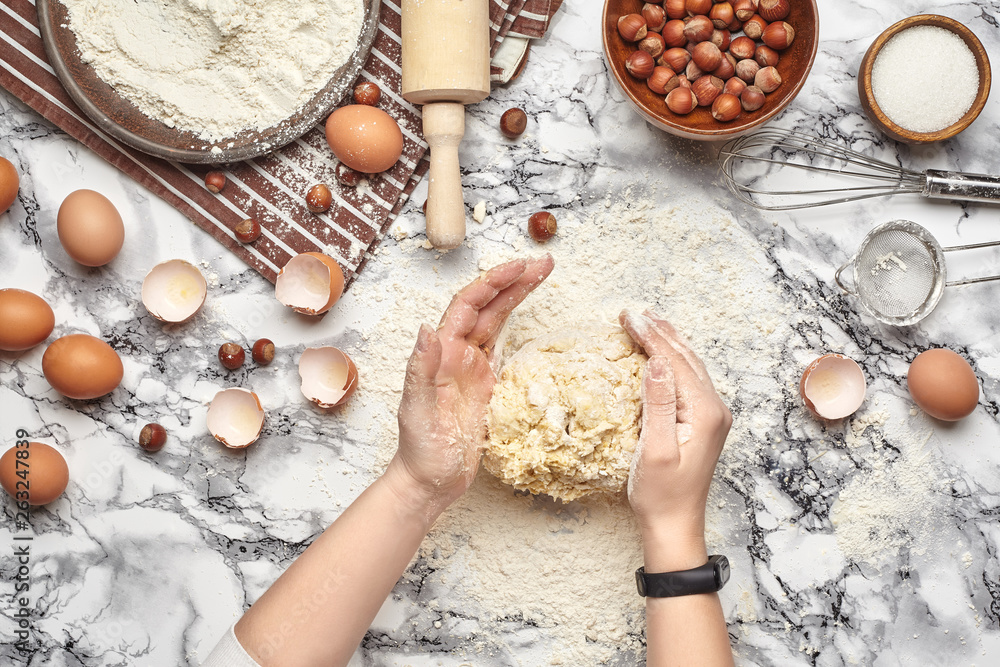 Fototapeta premium Close-up shot. Top view of a baker cook place, hands are working with a raw dough on the marble table background.