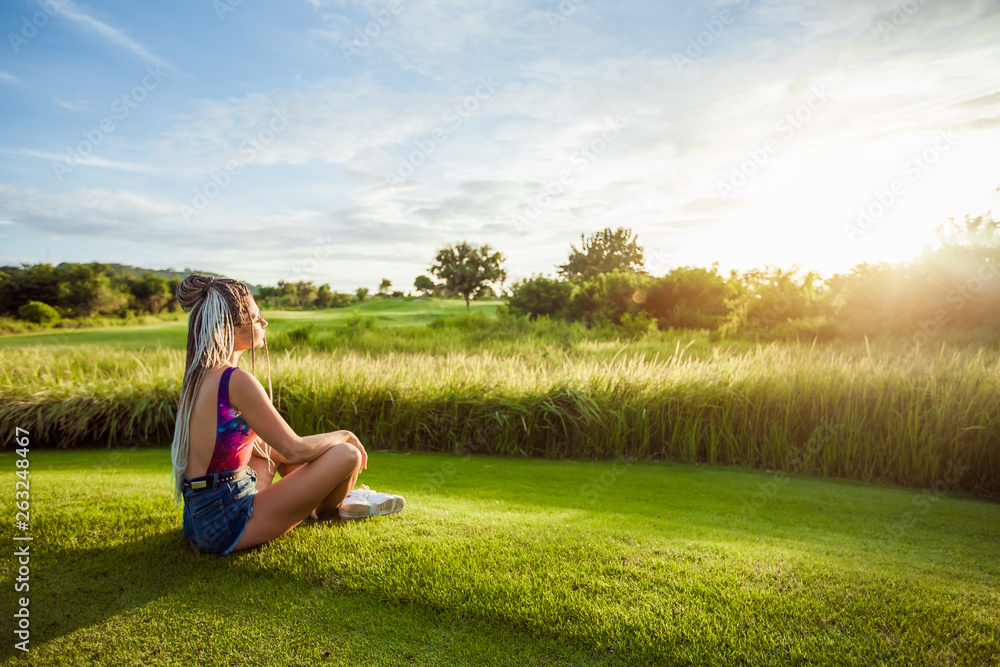 Girl with African braids sitting on the lawn and watching the sunset. copy space Girl with African braids sitting on the lawn and watching the sunset. copy space