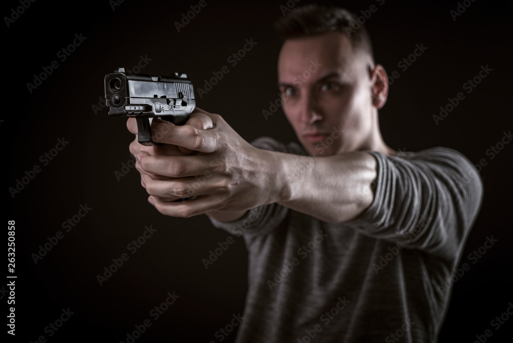 A young teenage man holding and aiming a gun sideways, black background A young teenage man holding and aiming a gun sideways, black background