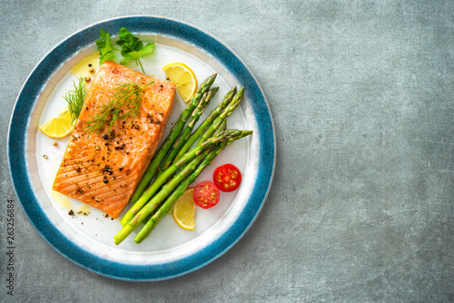 Grilled salmon steak garnished with green asparagus, lemon and tomatoes