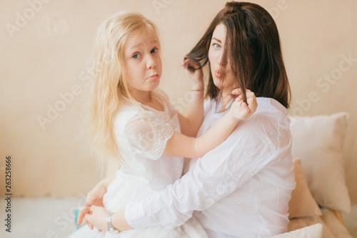 Mother and daughter indoor lifestyle portrait. Mom with child have fun on abstract background. Happiness of motherhood. Mother hugs with her little daughter. Young emotional girl  playing with mom.