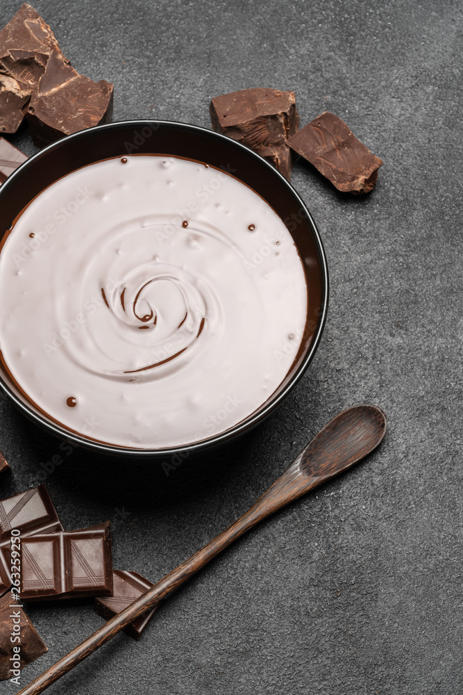 Fototapeta premium ceramic bowl of chocolate cream or melted chocolate and pieces of chocolate isolated on dark concrete background