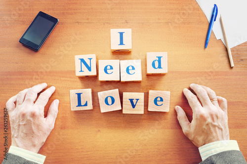 I need love. Businessman made text from wooden cubes on a desk
