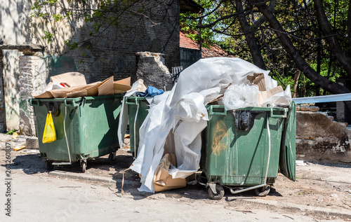 Big dumpster garbage cans full of overflow litter polluting the street in the city with junk and trash