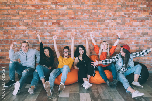 Yes. Group of excited millennials sitting on bean bags. Hands up. Support and approval gesture. Leisure at loft lounge area. photo