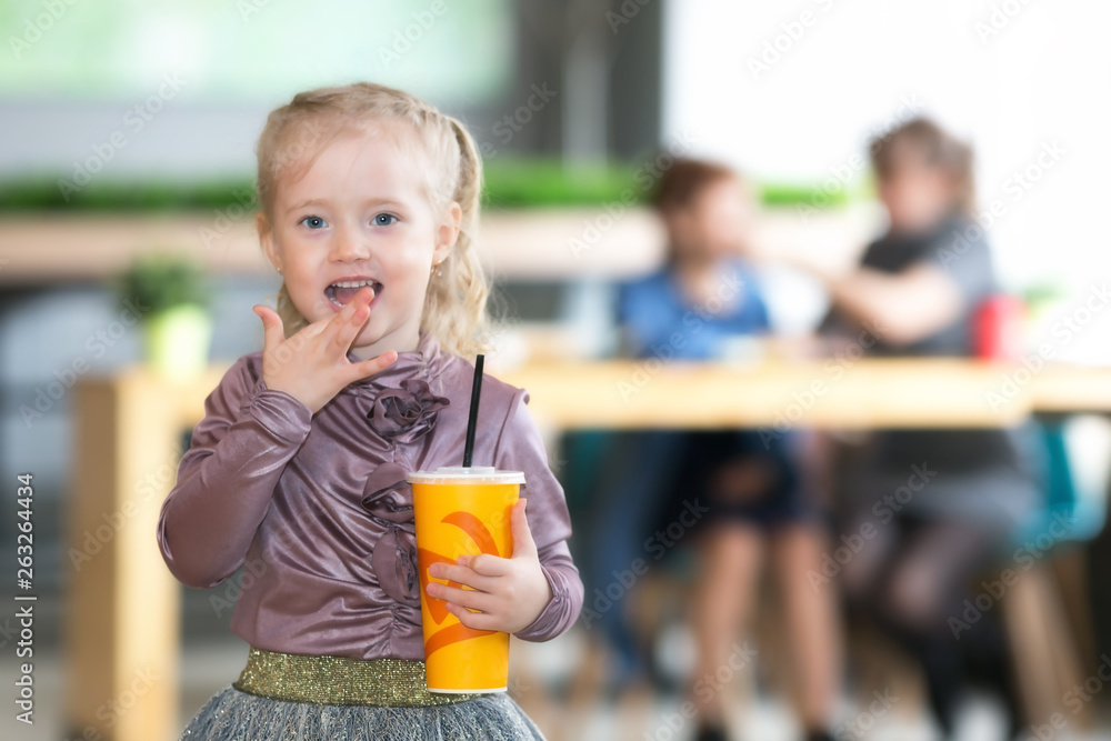 The girl drinks juice on the background oA small child alone drinks a cocktail from the tub and the mother and grandmother are talking from behind. A child without supervision, indifference of parents The girl drinks juice on the background oA small child alone drinks a cocktail from the tub and the mother and grandmother are talking from behind. A child without supervision, indifference of parents