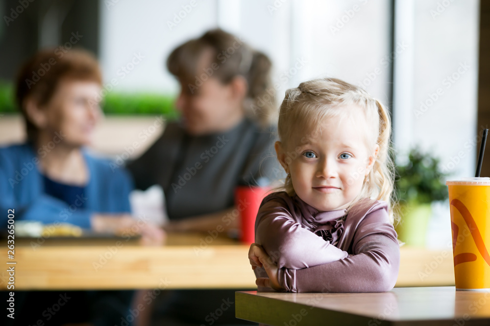 A little girl without parental supervision. The child was left alone in the cafe while mother grandmother were talking to each other. A little girl without parental supervision. The child was left alone in the cafe while mother grandmother were talking to each other.