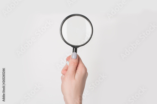 Female hand holding magnifier isolate on light background.