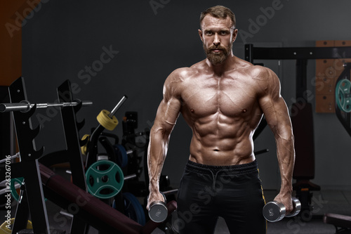 Muscular man in gym with dumbbells. Strong male naked torso abs, workout