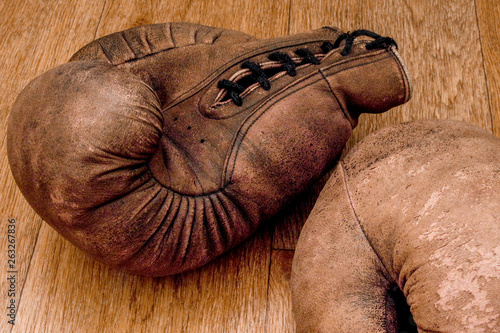 Boxing gloves. Old vintage retro pair of leather worn mittens are on the wood table. Red colors and soft lights. Gloves of retired boxer and fighter