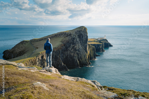  Tourist enjoys on peak of rock empire. Dreamy landscape, spring orange pink sky. Neist Point and lighthouse on sunny day in Scottish Highlands, UK. photo