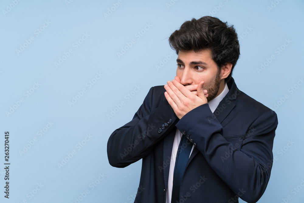 Businessman over isolated blue wall covering mouth and looking to the side Businessman over isolated blue wall covering mouth and looking to the side