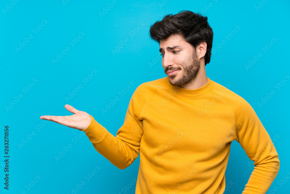 Handsome over isolated blue wall holding copyspace with doubts Handsome over isolated blue wall holding copyspace with doubts