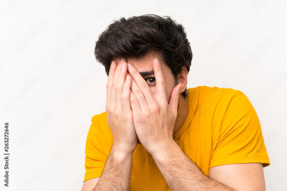 Handsome over isolated white wall covering eyes and looking through fingers Handsome over isolated white wall covering eyes and looking through fingers