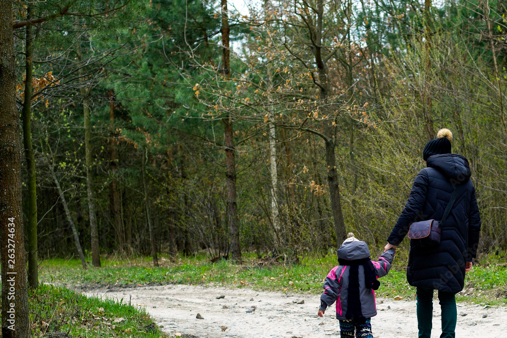 Mother and daughter are walking in the spring forest. baby and mother walk along the forest road by the hand Mother and daughter are walking in the spring forest. baby and mother walk along the forest road by the hand