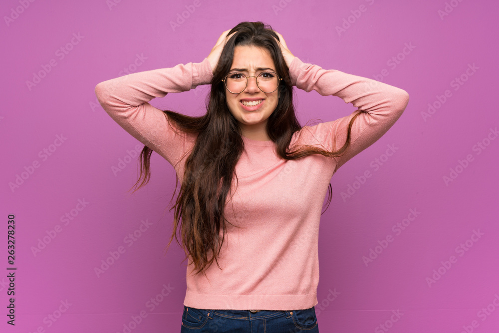 Teenager girl over purple wall frustrated and takes hands on head Teenager girl over purple wall frustrated and takes hands on head