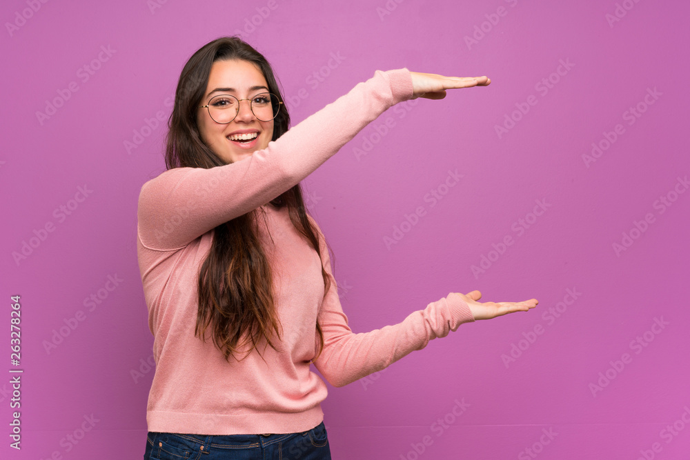 Teenager girl over purple wall holding copyspace to insert an ad Teenager girl over purple wall holding copyspace to insert an ad