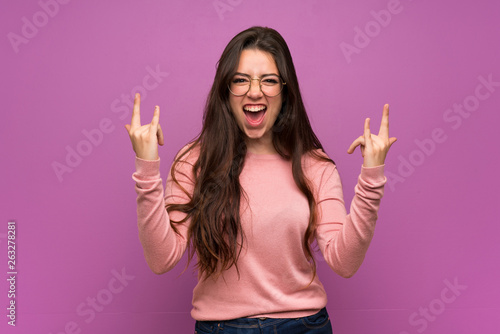 Teenager girl over purple wall making rock gesture