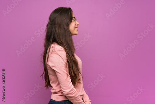 Teenager girl over purple wall in lateral position