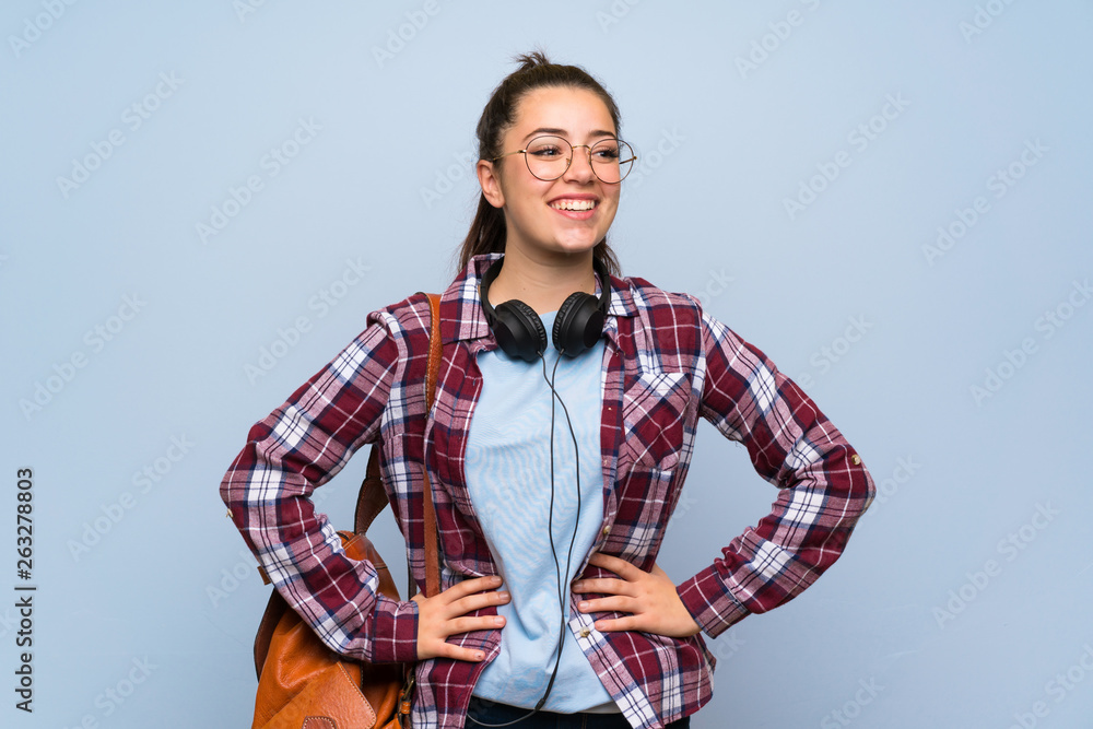 Teenager student girl over isolated blue wall posing with arms at hip and smiling Teenager student girl over isolated blue wall posing with arms at hip and smiling