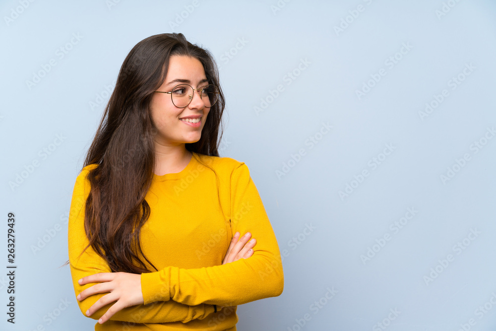 Teenager girl over isolated blue wall standing and looking to the side Teenager girl over isolated blue wall standing and looking to the side