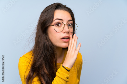 Foto Teenager girl over isolated blue wall whispering something