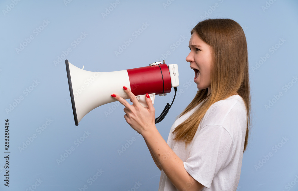 Young woman over blue wall shouting through a megaphone Young woman over blue wall shouting through a megaphone