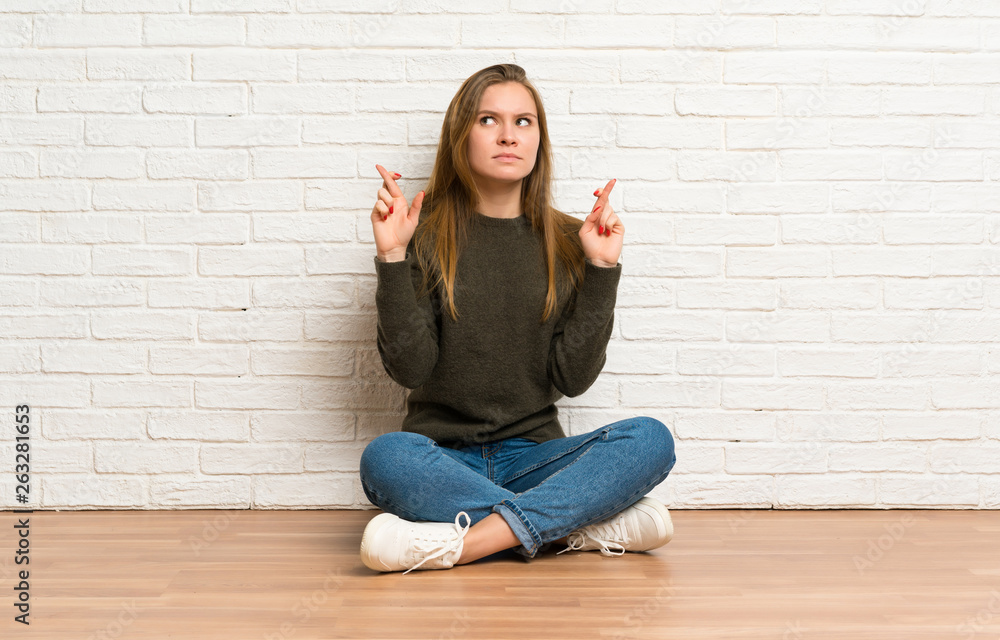 Young woman sitting on the floor with fingers crossing and wishing the best Young woman sitting on the floor with fingers crossing and wishing the best