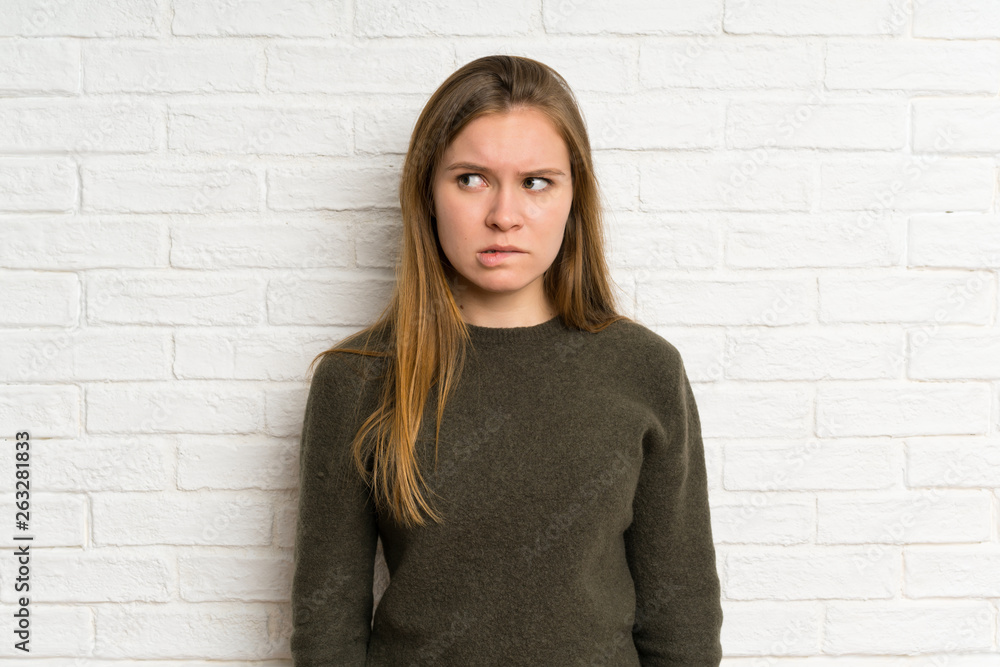 Young woman over white brick wall having doubts and with confuse face expression Young woman over white brick wall having doubts and with confuse face expression
