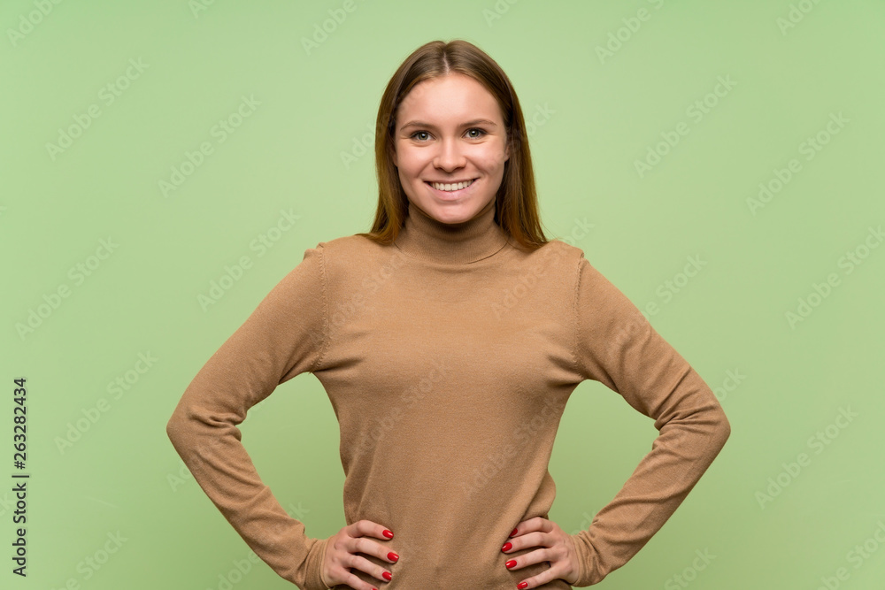 Obraz premium Young woman with turtleneck sweater posing with arms at hip and smiling