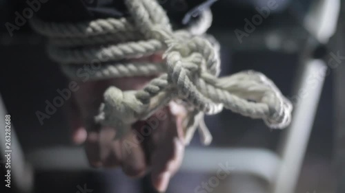 Close up of human hands tied with white colored rope and sitting on a metal chair. photo