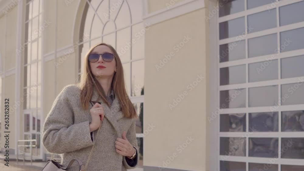 Stylish lady is strolling alone outdoors in city, wrapping in coat Stylish lady is strolling alone outdoors in city, wrapping in coat