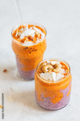 Orange and purple vegan smoothie is made from blueberry, sea buckthorn, coconut cream, nuts and chia on a white background. The concept of healthy summer food and drink.